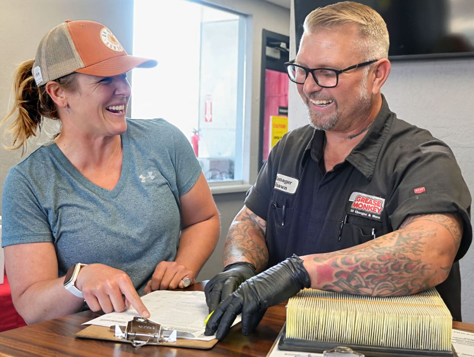 Grease Monkey manager reviews manufacturer recommended services with a smiling customer